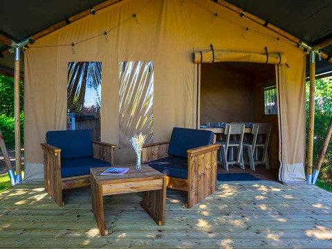 Safari tent Slow Lodge at Camping Seasonova La Forêt, France, with wooden deck, chairs, and open dining space.