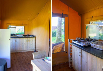 Interior of safari tent at Slow Lodge, Camping Seasonova La Forêt, France, with kitchen and wooden floor.