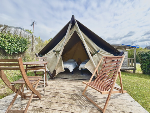 Glamping accommodation with a canvas tent, two single beds, and wooden chairs on a deck outdoors.
