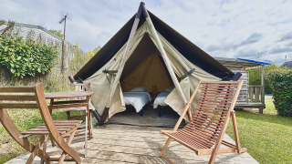Alojamiento glamping con tienda de campaña, dos camas individuales y muebles de madera en la terraza.