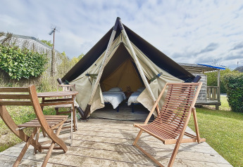 Glampingverblijf met tent, twee enkele bedden en houten buitenmeubels op een houten terras.