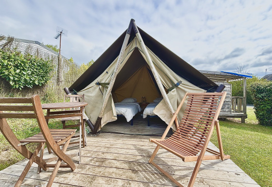 Alojamiento glamping con tienda de campaña, dos camas individuales y muebles de madera en la terraza.