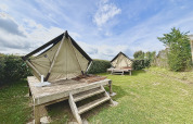 Two glamping tents set on wooden decks in a grassy outdoor area under a partly cloudy blue sky.