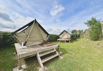 Twee glamping tenten op houten terrassen in een grasrijke buitenruimte met een blauwe, bewolkte lucht.