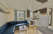Modern glamping accommodation with blue L-shaped sofa, compact kitchen, and window with colorful curtains.