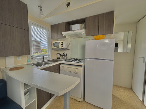 Modern small kitchen in glamping accommodation with stove, fridge, microwave, and storage cabinets.