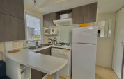 Modern small kitchen in glamping accommodation with stove, fridge, microwave, and storage cabinets.