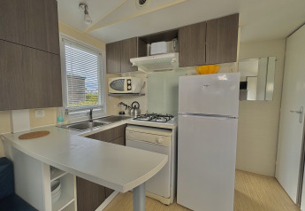Modern small kitchen in glamping accommodation with stove, fridge, microwave, and storage cabinets.
