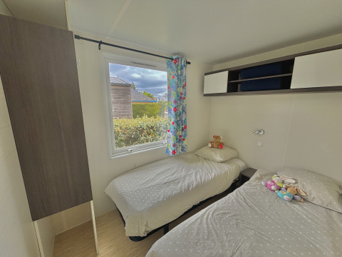 A cozy glamping room with two single beds, floral curtain, wall storage, and plush toys on the beds.