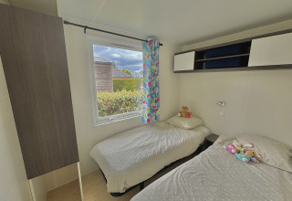 A cozy glamping room with two single beds, floral curtain, wall storage, and plush toys on the beds.