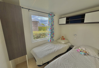 A cozy glamping room with two single beds, floral curtain, wall storage, and plush toys on the beds.