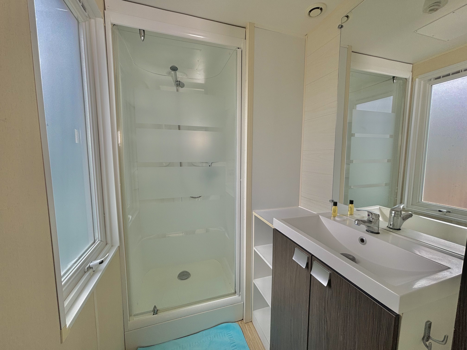 Moderne badkamer met douchecabine, grote spiegel, wastafel en ramen bij een glampingaccommodatie.