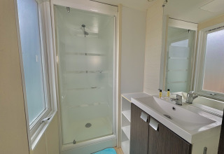 Modern bathroom with shower cabin, large mirror, sink, and windows at a glamping accommodation site.