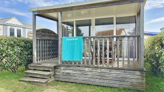 Cabaña de madera Cottage Zen con porche cubierto, puertas de cristal, toalla y setos verdes alrededor.