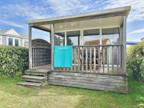 Cabaña de madera Cottage Zen con porche cubierto, puertas de cristal, toalla y setos verdes alrededor.