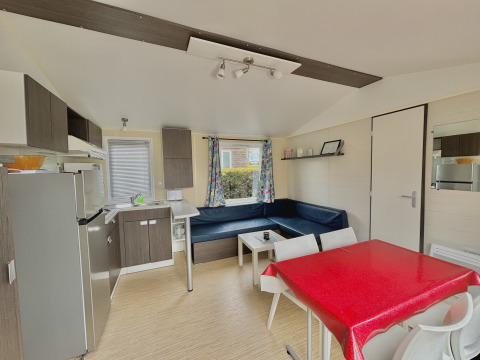 Alojamiento glamping luminoso y moderno con cocina, mesa de comedor, sofá rinconero y cortinas coloridas.