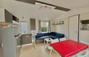 Bright, modern glamping accommodation interior with kitchen, dining table, corner sofa, and colorful curtains.