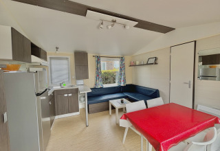 Bright, modern glamping accommodation interior with kitchen, dining table, corner sofa, and colorful curtains.