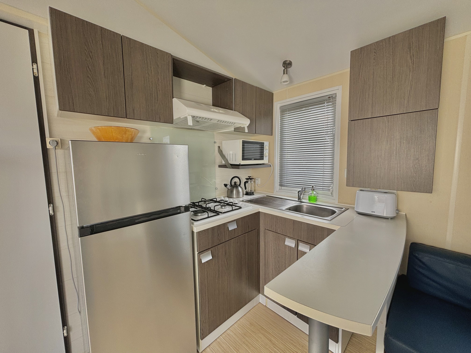 Moderne glampingkeuken met koelkast, gasfornuis, magnetron, spoelbak en houten kasten in een kleine ruimte.