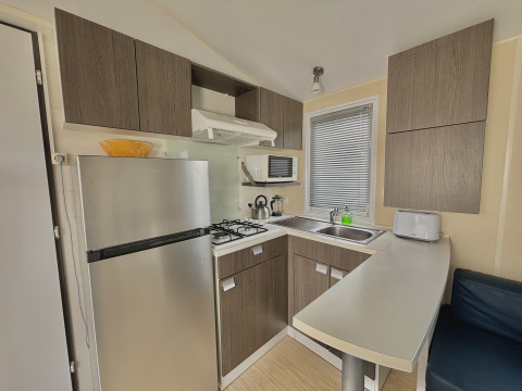 Cucina moderna da glamping con frigorifero, fornello a gas, microonde, lavello e mobili in legno.