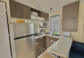 Cucina moderna da glamping con frigorifero, fornello a gas, microonde, lavello e mobili in legno.