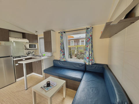 Interior view of a glamping accommodation with blue corner sofa, small kitchen, and floral window curtains.