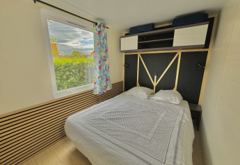 Glamping bedroom with large bed, overhead storage, window view of greenery, and colorful curtain.