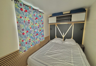 Bedroom in Cottage Zen at Camping Seasonova Le Point du Jour, France, with floral curtains and double bed.