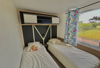 Habitación de glamping luminosa con dos camas individuales, peluches, cortinas coloridas y vista al jardín.