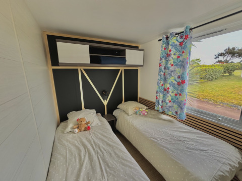 Stanza glamping luminosa con due letti singoli, peluche, tende colorate e vista su un giardino verde.