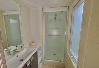 Bagno moderno con doccia, lavandino e grande finestra in un alloggio glamping con luce naturale.