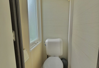 Baño compacto moderno con inodoro, ventana esmerilada y suelo símil madera en alojamiento glamping.