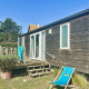 Træhytte Cottage Evasion med terrasse og liggestol under blå himmel, omgivet af grønne planter.