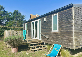 Cottage Evasion wooden cabin with deck and sun lounger under a blue sky, surrounded by greenery.