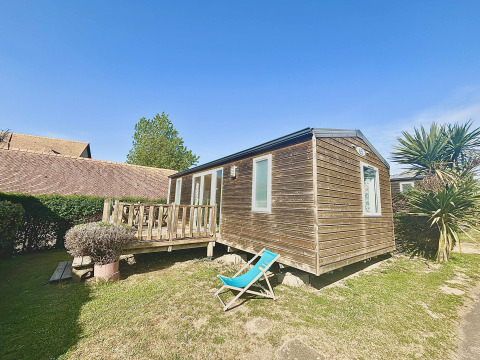 Cabaña de madera con terraza y silla reclinable en Cottage Evasion, Camping Seasonova Le Point du Jour, Francia.