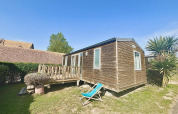Wooden cabin with a deck and a lounge chair at Cottage Evasion, Camping Seasonova Le Point du Jour, France.