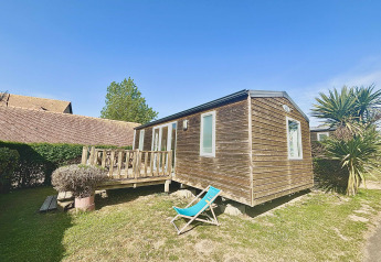 Cabaña de madera con terraza y silla reclinable en Cottage Evasion, Camping Seasonova Le Point du Jour, Francia.