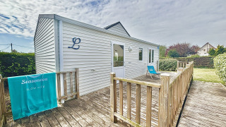 Cottage PMR adapté aux personnes handicapées, terrasse en bois, transat bleu, jardin verdoyant.