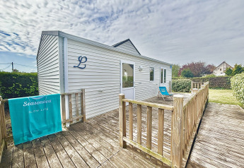 Cottage PMR adapté aux personnes handicapées, terrasse en bois, transat bleu, jardin verdoyant.