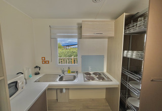 Cuisine accessible d’un cottage PMR en France avec plaques de cuisson, évier, étagères et vaisselle.