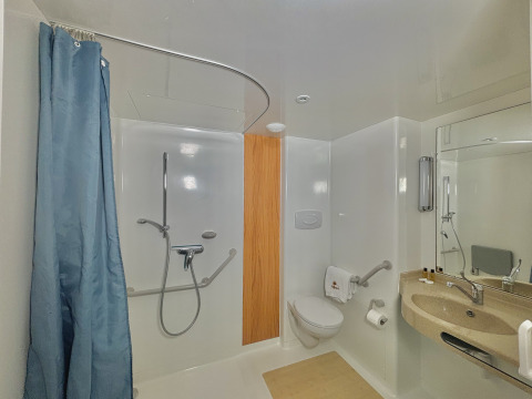 Baño accesible con ducha abierta, barras de apoyo, inodoro elevado y lavabo adaptado para usuarios de silla de ruedas.