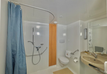 Bagno accessibile con doccia aperta, maniglioni di supporto, WC rialzato e lavandino ribassato per disabili.