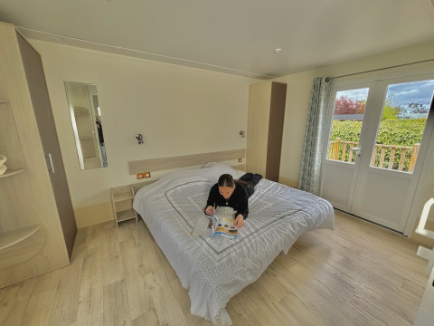Person reading a magazine on a bed in an accessible cabin at Camping Seasonova Le Point du Jour in France.