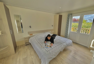 Person reading a magazine on a bed in an accessible cabin at Camping Seasonova Le Point du Jour in France.