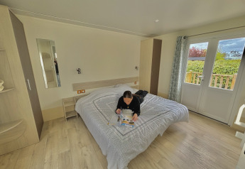 Personne lisant un magazine sur un lit dans un cottage PMR au Camping Seasonova Le Point du Jour en France.