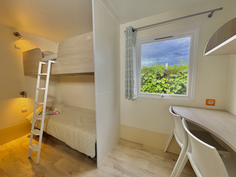 Helles Zimmer mit Etagenbetten, Schreibtisch und Fenster im Cottage PMR auf Camping Seasonova Le Point du Jour.
