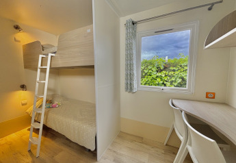 Lichte kamer met stapelbedden, bureau en raam in Cottage PMR op Camping Seasonova Le Point du Jour, Frankrijk.