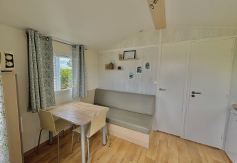 Salon lumineux et épuré du Cottage Zen au Camping Seasonova Le Point du Jour, France, avec table et banquette.