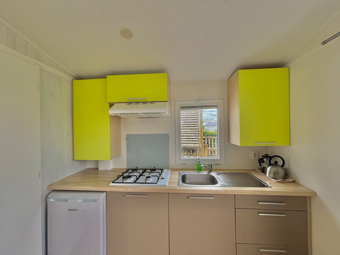 Moderne Küche im Cottage Zen auf Camping Seasonova Le Point du Jour, Frankreich, mit grünen Schränken.