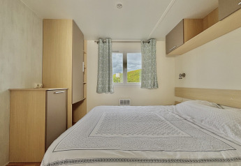 Slaapkamer met dubbel bed, lichte gordijnen en natuurzicht in Cottage Zen, Camping Seasonova Le Point du Jour.